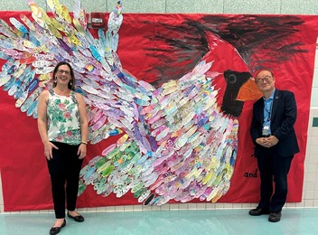 Lady and man stand in front of a cardinal mural made from student created feathers
