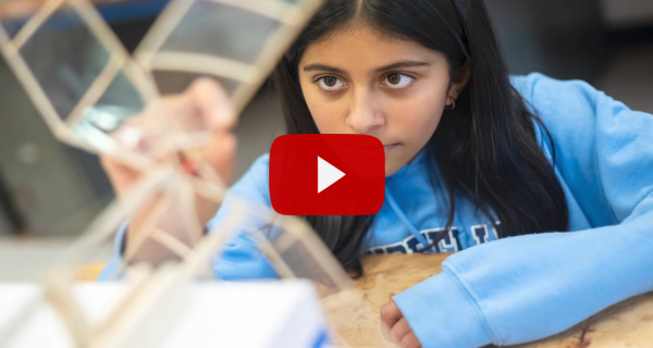 A playbutton superimposed over an image of a student working on a project 