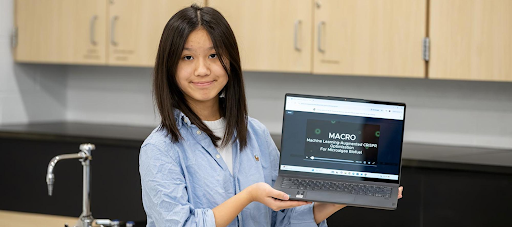 A girl holds up a laptop.