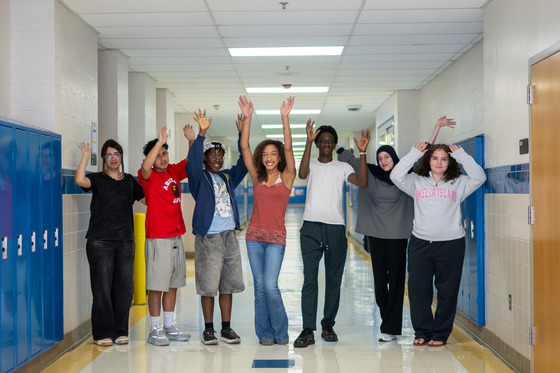 High schoolers hold their hands up and smile in a school hallway