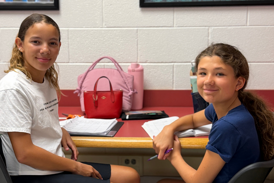 two girls sit in the library together smiling