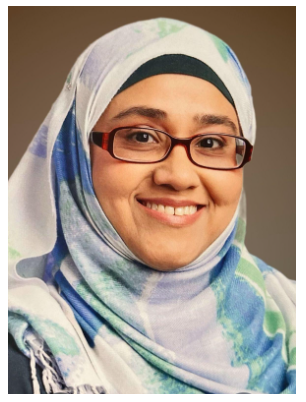 A smiling woman wearing  glasses and a light blue, green patterned hijab