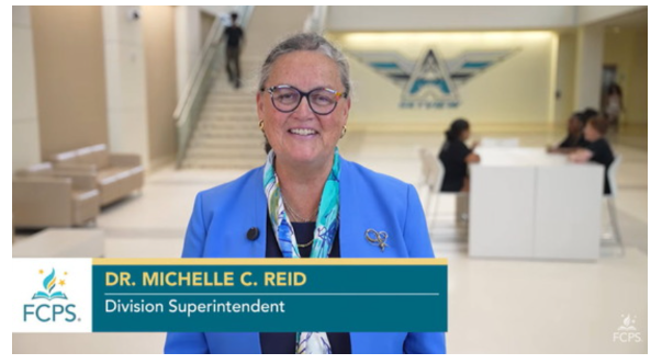 The image shows Dr. Michelle C. Reid, identified as a Division Superintendent for FCPS, smiling in a bright school or office lobby