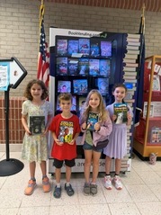 Four students standing in front of a vending machine holding books in their hands.