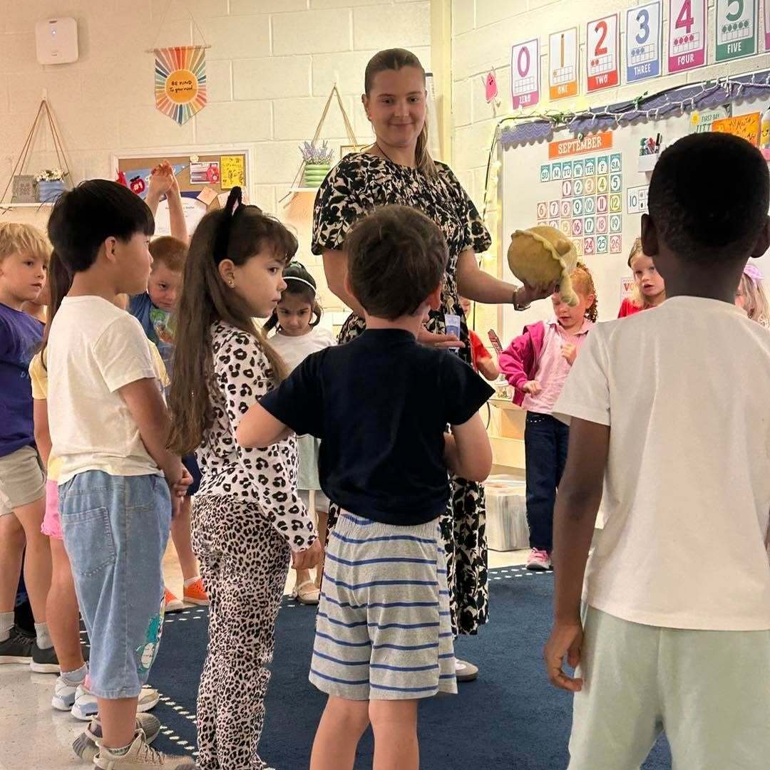 Students gather around a teacher holding a large object during a morning meeting.