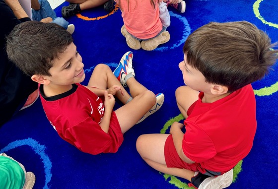 Two students sitting on a rug having a conversation.