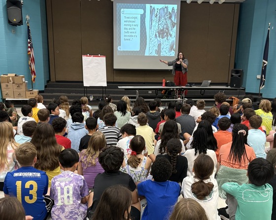 Picture of 5th grade students seated and listening to a presentation by a guest author
