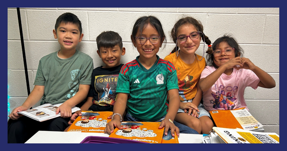 Five students squished on a small sofa smile at the camera with their orange Benchmark materials in their hands.