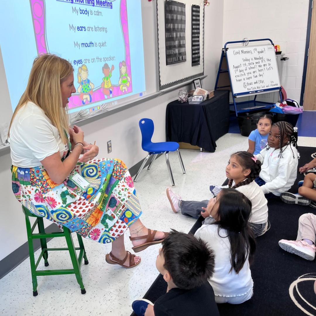 Mrs. Tickle talks to her students, who are sitting on the carpet.