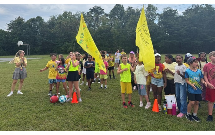 4th grade students wearing yellow holding their flag and cheering at the pep rally