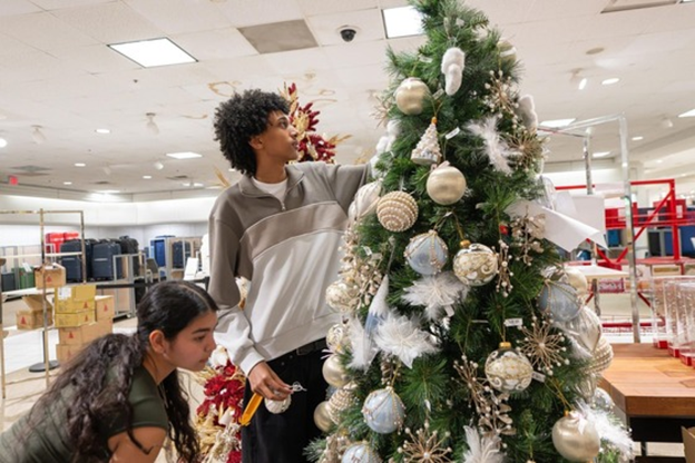 Chantilly Academy students decorating a tall Christmas tree inside a retail store.