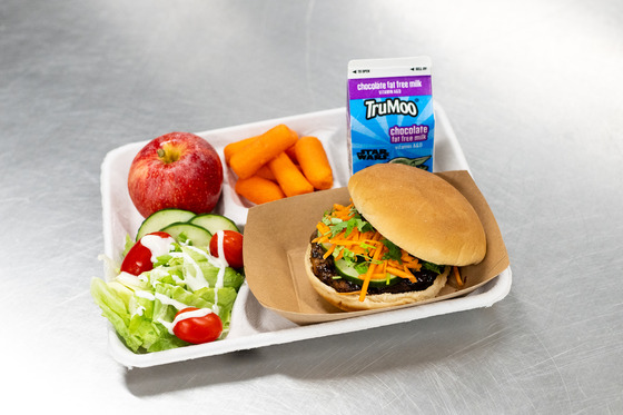 Photo of lunch tray with milk, carrots, salad, apple and a banh mi burger
