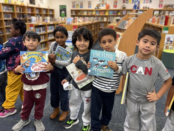 Five kindergarten students smile and hold books they selected from the school library.