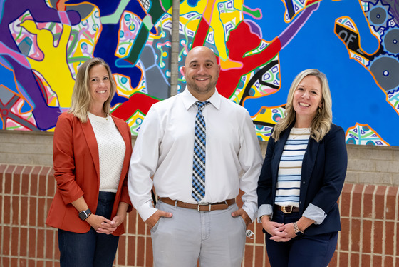 three people standing side by side with a colorful painting behind them in the background