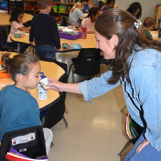 A picture of a teacher holding a cup to the student to learn about sense of smell