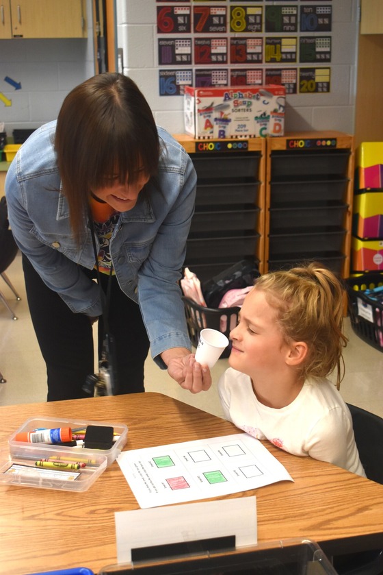 A picture of a teacher holding a cup to the student to learn about sense of smell