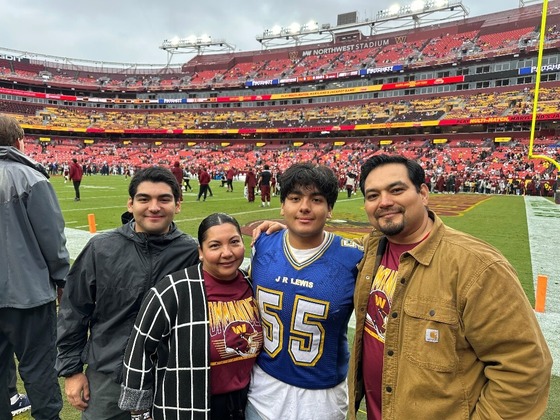 Image of two students one student in a blue jersey with the number 55 with two adults at a football game