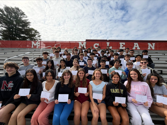 A large group of McLean High School students posed on outdoor bleachers holding certificates