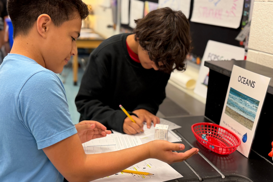 Two students work on their Carbon Cycle Passports at the Oceans station, rolling dice to determine where their carbon atoms travel next.