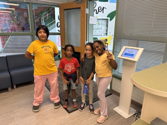 Four students stand in the front office area with a smile