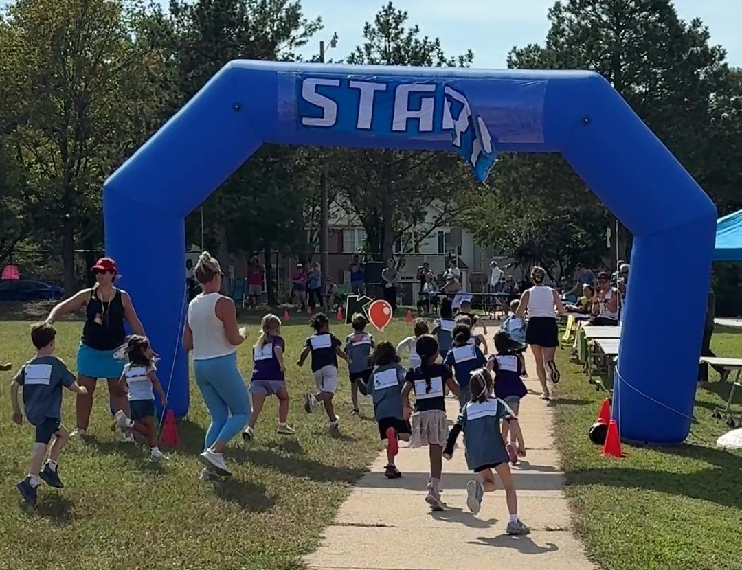Students, teachers, and parents running through the start gate at the Fun Run