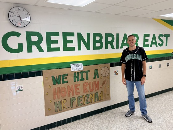 Principal Mr. Pietzman smiles beside a teacher-made sign reading, “We hit a home run with Mr. Pietzman!”