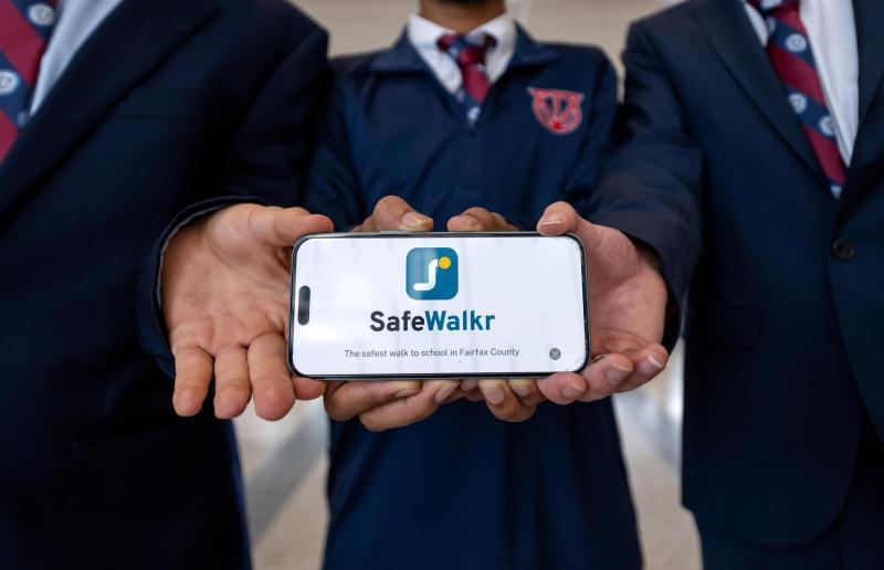 The students display their app, SafeWalkr, on a cell phone.
