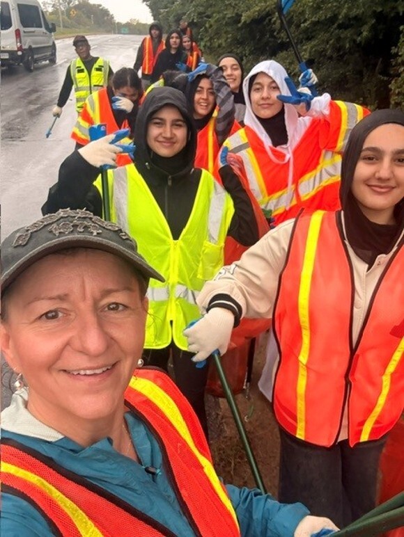 Students and two teachers with orange and yellow vest with cleaning tools on the highway