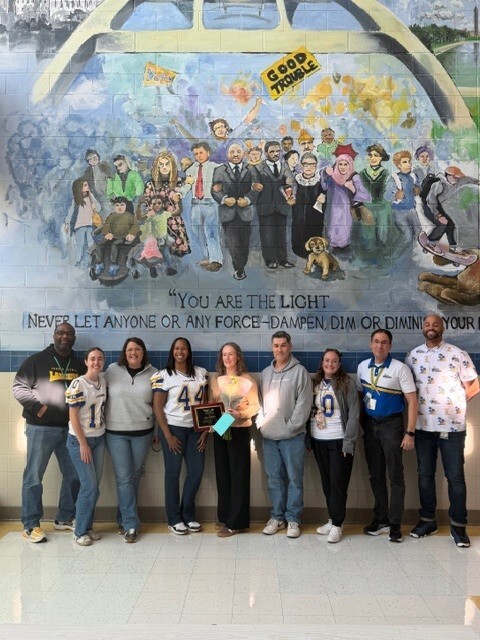 Faculty members standing in the lobby in front of a  mural 