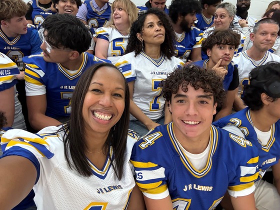 Teachers and principal with students in blue and yellow jerseys at homecoming