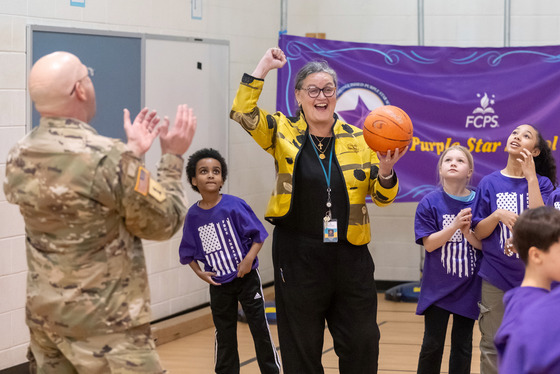 A woman cheers, holding a basketball, with kids wearing purple looking on. 