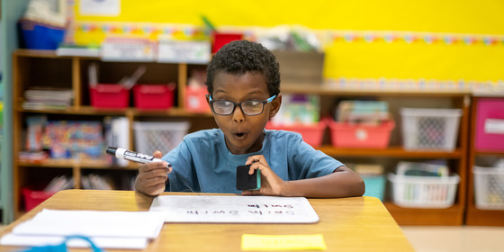 A boy writing on a white board has an excited face. 