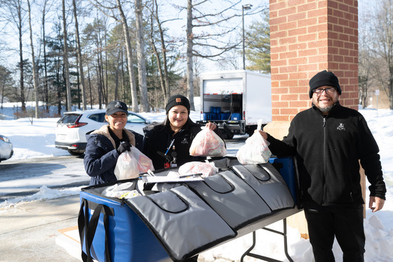 Three workers take bagged food out of coolers outdoors in the snow. 