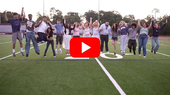 High school students holding hands and jumping into the air together on a football field on the first day of school.