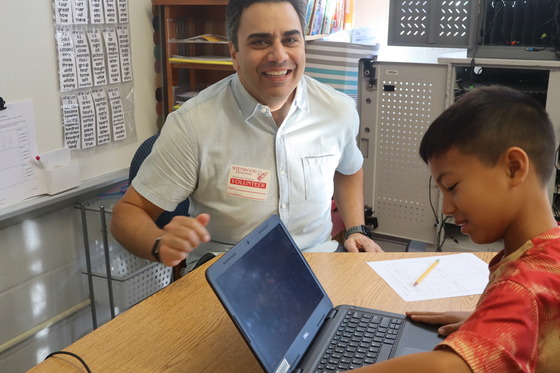 A 2nd grader wearing a red shirt on the computer showing his parent his work