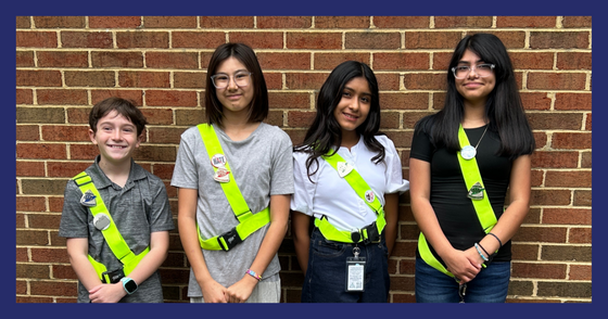Four students wearing Safety Patrol sashes and officer pins smile after their induction ceremony.