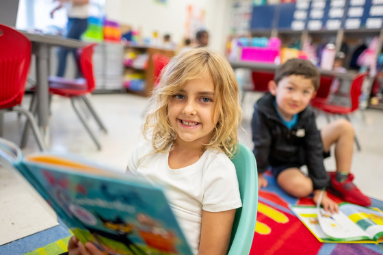 Two students sitting on a colorful classroom carpet with books in their laps
