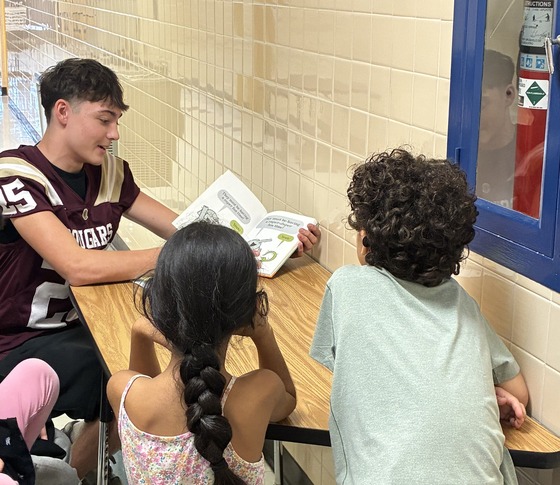 football student reading to elementary students