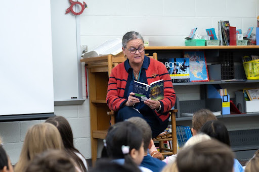 Dr. Reid sits in a rocking chair reading to students.