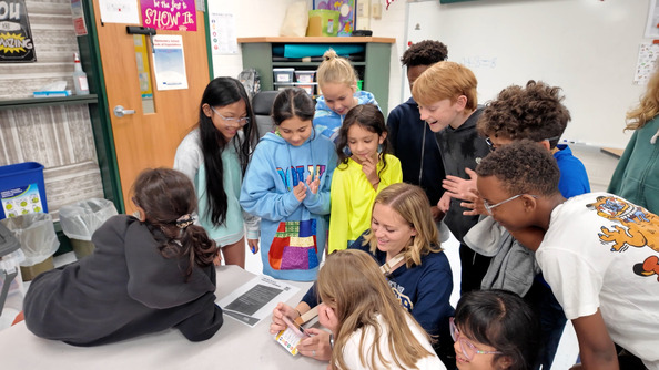 Elementary students standing around teacher at a big desk