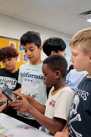 Students at a desk surrounding a tablet 