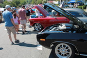 People looking at a row of antique cars with their hoods up