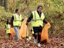 Kids in yellow vest collecting orange bags of litter in the forest