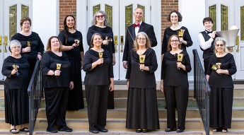 Two rows of people dressed in formal black attire holding handbells and smiling at the viewer