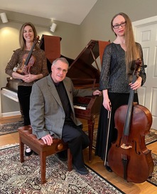 man sitting at the piano with two women standing on either side of him, one holding a violin and the other a cello