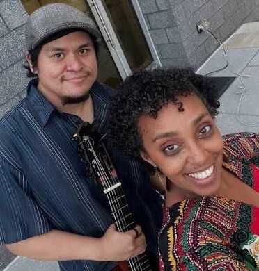 man with a gray hat and guitar and a woman smiling at the camera with colorful dress
