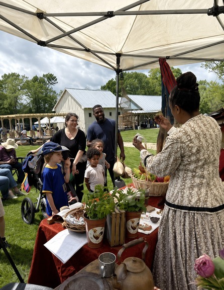 Image of interpreter in period clothes holding an object in front of a family while under a tent on the lawn at Historic Blenheim