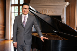 Alfred Yun standing by a black grand piano smiling at the viewer 