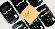 Photo of six calculators with a post-it note sitting on top with the message "Tax Season." 