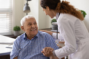 Photo of an older man holding hands with and smiling at a woman wearing a white lab coat. 